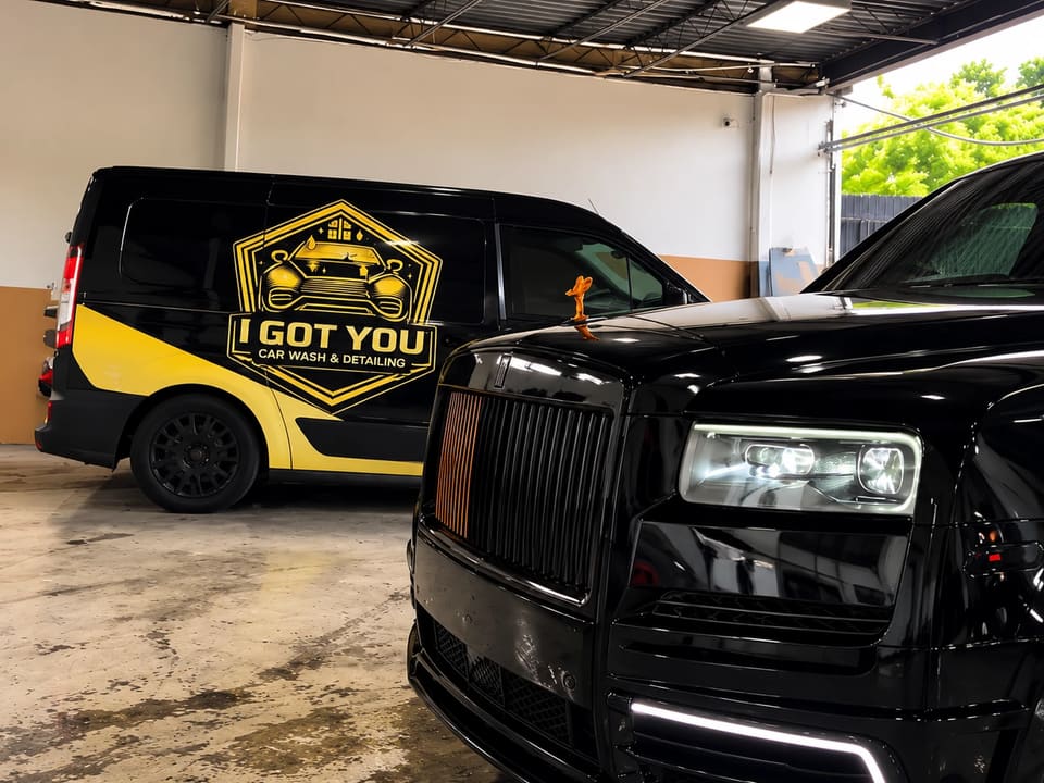 The I Got You van parked beside the front of a black Rolls-Royce Cullinan.